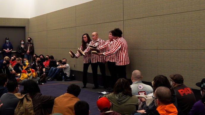 A classic barbershop quartet, dressed in red and white striped suits, holding their wicker hats out in front of them surrounded by people in a crowded room